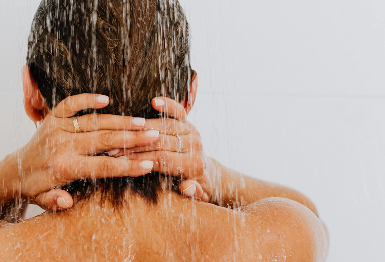 back of a woman's head in the shower with her hands clasped behind her neck